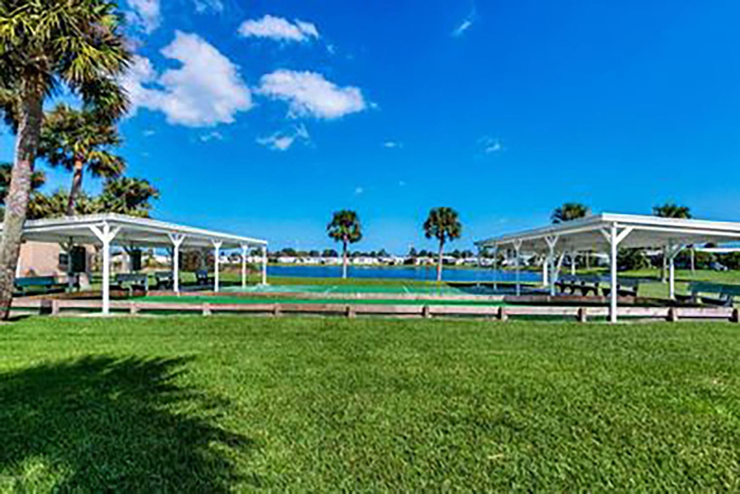 Lush green lawn with two shaded pavilions overlooks a serene lake under a bright blue sky, ideal for outdoor gatherings and relaxation.