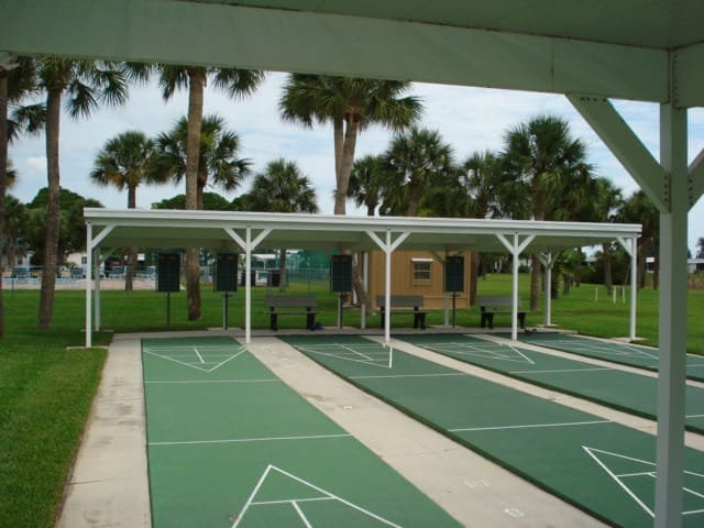 Outdoor shuffleboard courts with shaded areas, surrounded by palm trees, offering a recreational space in a sunny environment.