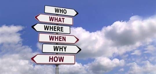 Directional signpost displaying the words "Who," "What," "Where," "When," "Why," and "How" against a blue sky with clouds, symbolizing exploration and inquiry.